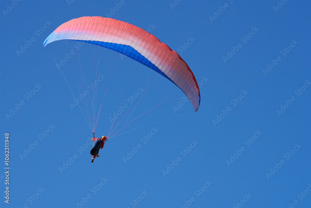 Paraglider under red and blue dome in blue sky. Copy space. Paraglider under red and blue dome in blue sky. Copy space.