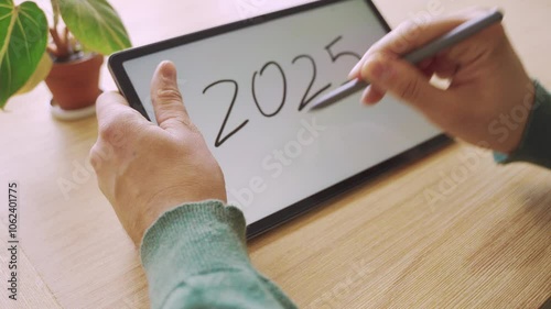 New year's resolutions. Hand with pen writing in tablet 2025