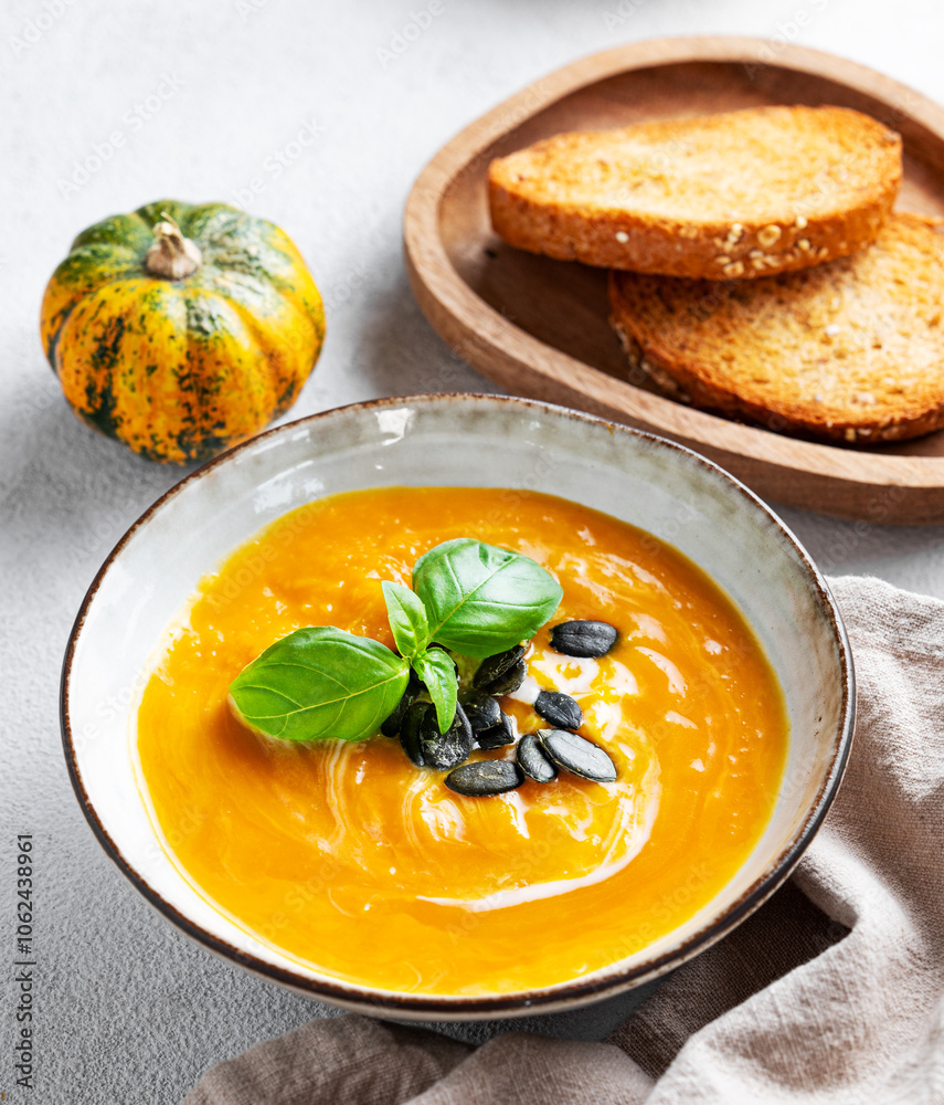 Pumpkin soup with cream, basil and seeds on a light background with bread and napkin close up. Pumpkin soup with cream, basil and seeds on a light background with bread and napkin close up.