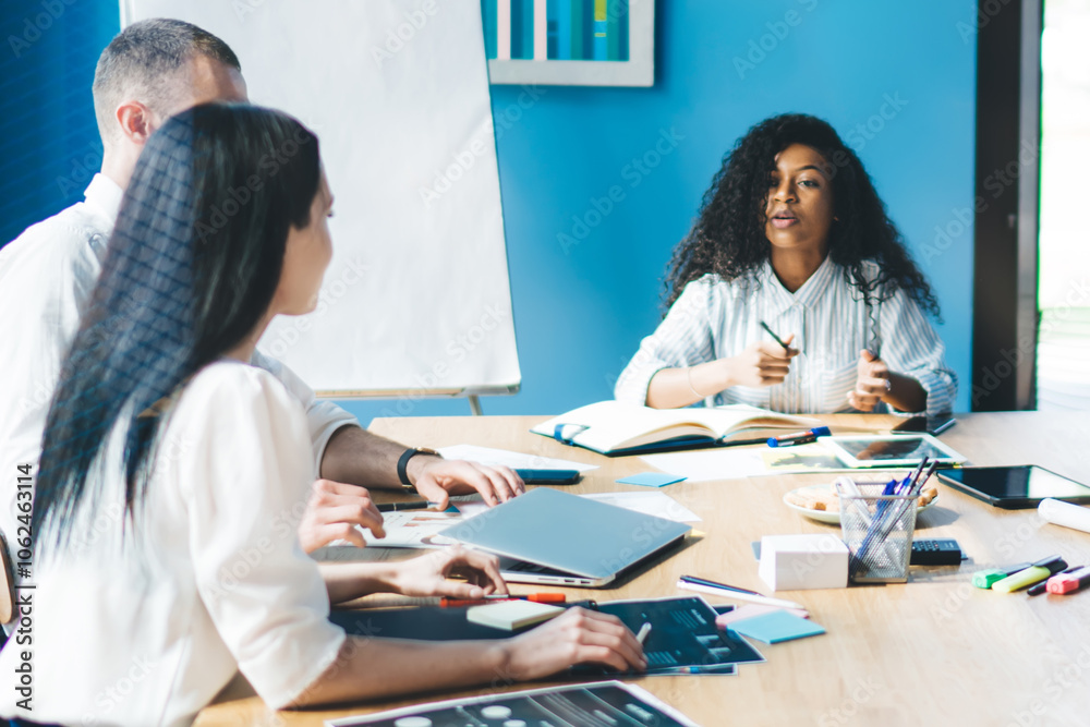 Obraz premium Attentive multiethnic office workers discussing graphs while sitting at table