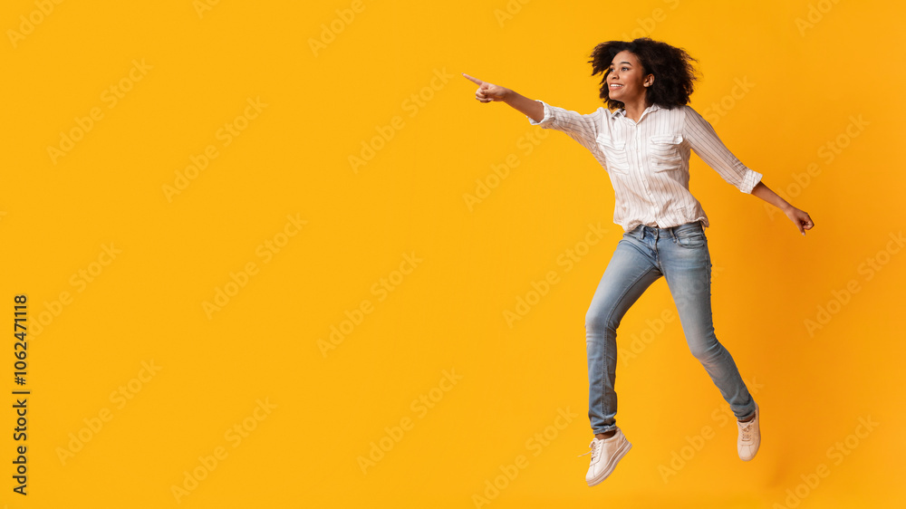 Look there. Excited Afro Woman Jumping And Pointing Aside At Copy Space On Yellow Background, Full-Lenght