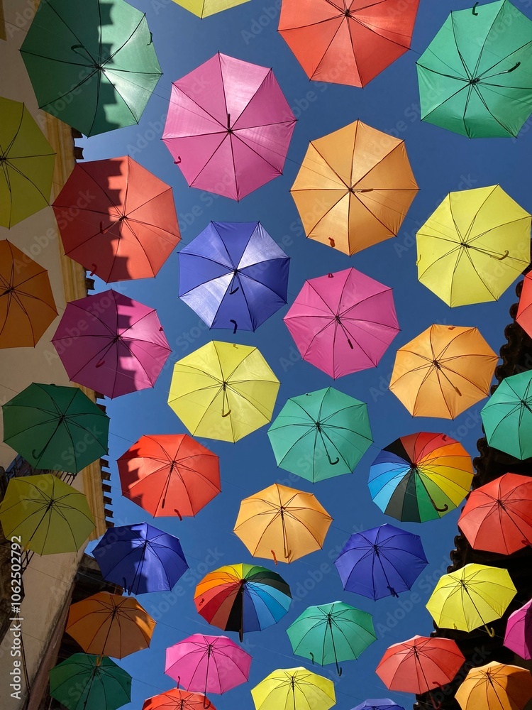 Naklejka premium Bright and colourful umbrellas hanging above buildings