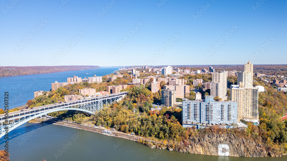 Fototapeta premium This location in the Bronx offers stunning views of lush greenery, a picturesque lake, and urban structures. Framed by the river, it showcases iconic bridges and the New York City skyline 