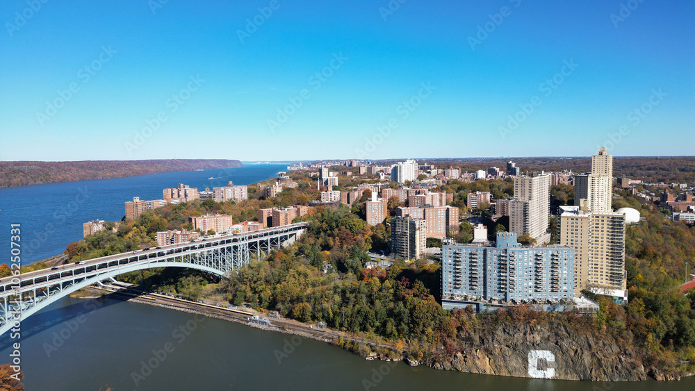Fototapeta premium This location in the Bronx offers stunning views of lush greenery, a picturesque lake, and urban structures. Framed by the river, it showcases iconic bridges and the New York City skyline 
