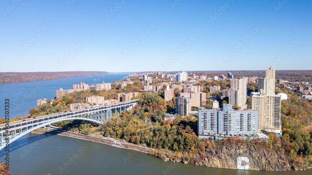 Fototapeta premium This location in the Bronx offers stunning views of lush greenery, a picturesque lake, and urban structures. Framed by the river, it showcases iconic bridges and the New York City skyline in the dista