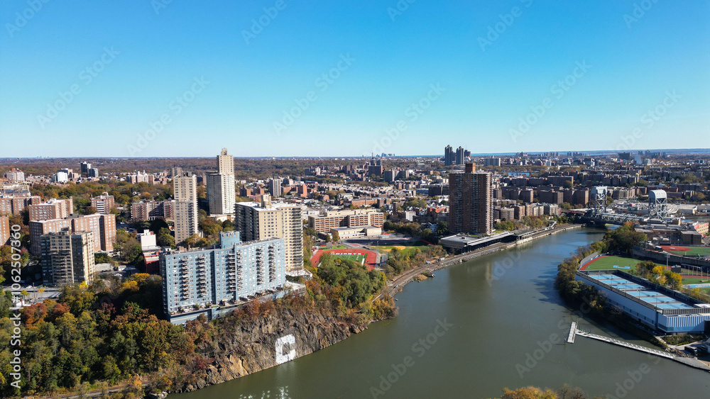 Fototapeta premium This location in the Bronx offers stunning views of lush greenery, a picturesque lake, and urban structures. Framed by the river, it showcases iconic bridges and the New York City skyline in the dista
