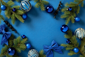 Christmas card. Frame of fir branches with blue balls and festive ornaments on a vibrant blue background