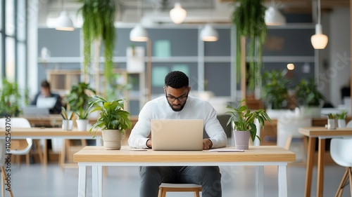 A focused man works on a laptop in a bright, plant-filled workspace, showcasing a blend of productivity and modern design.