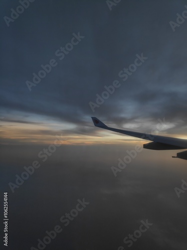 View from the airplane window showing a serene sky at sunset with the silhouette of the wingtip barely visible in the darkness