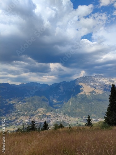 An expansive mountain landscape with an overcast sky, showcasing lush valleys and rugged peaks. Dense clouds create a dramatic and peaceful atmosphere in the scene.