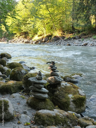 Artistic arrangement of stacked stones along a gentle river flow, embodying the tranquility and meditative state found in natural settings, amidst lushness.
