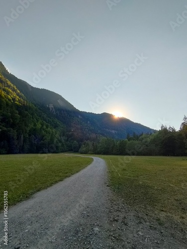 A captivating scene of a sunset over a mountain range casting golden rays over a lush green meadow, symbolizing tranquility and the beauty of untouched nature.