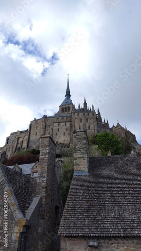 A majestic castle stands atop a hill, with a cloudy sky providing a dramatic backdrop. The intricate architecture reflects historical grandeur and medieval style.