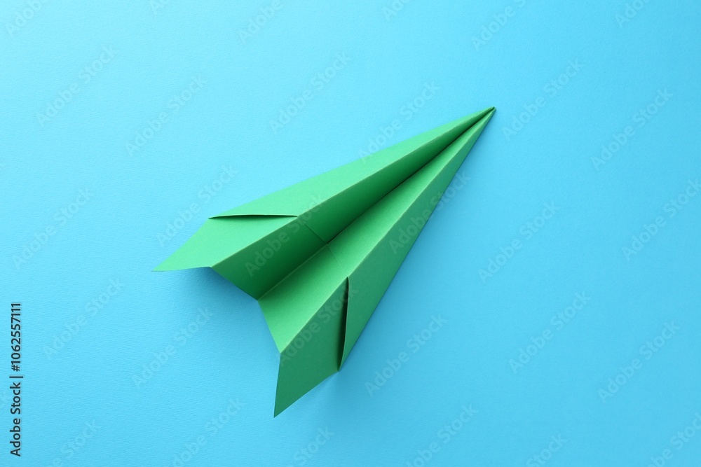 Naklejka premium One handmade green paper plane on light blue background, top view
