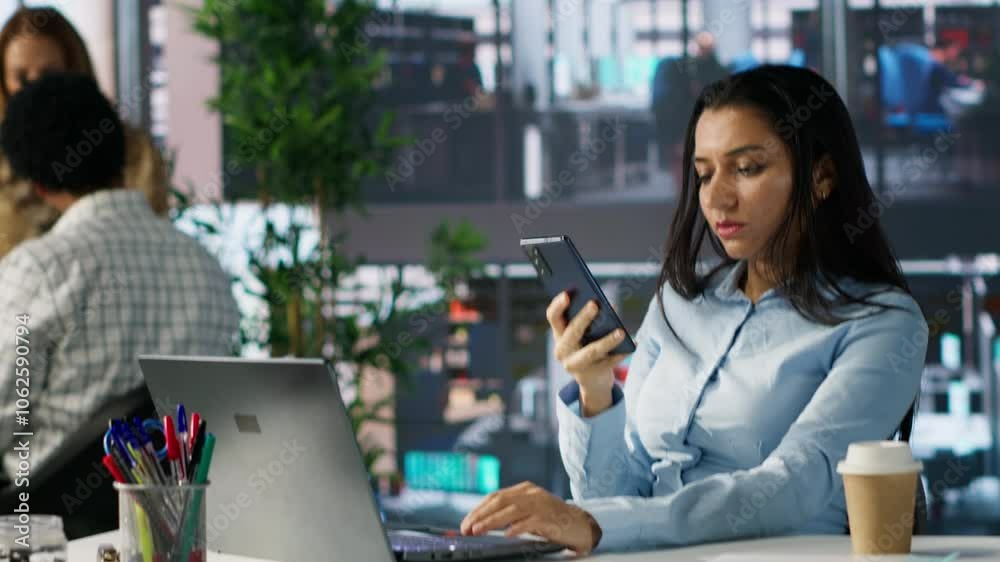 Entrepreneur uses her mobile phone for a crucial corporate communication. Woman discusses resource allocation, financial planning and deadline management while working on her laptop. Camera A.