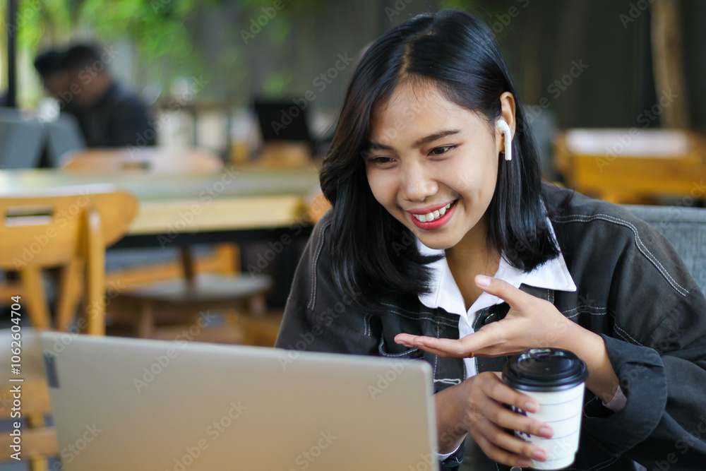 © M Alfan Setyawan - happy asian woman holding a cup of coffee and working on laptop have video conference in cafe with showing presenting gesture © M Alfan Setyawan - happy asian woman holding a cup of coffee and working on laptop have video conference in cafe with showing presenting gesture