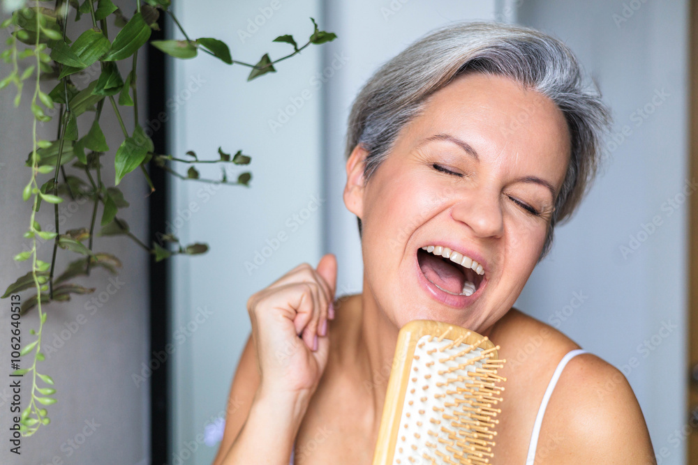 Beautiful middle-aged European woman with gray hair singing in the bathroom, using a wooden comb Beautiful middle-aged European woman with gray hair singing in the bathroom, using a wooden comb