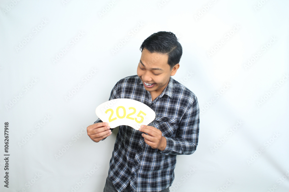 joyful asian man holding 2025 new years eve greeting card wearing casual plaid clothes isolated on white background joyful asian man holding 2025 new years eve greeting card wearing casual plaid clothes isolated on white background