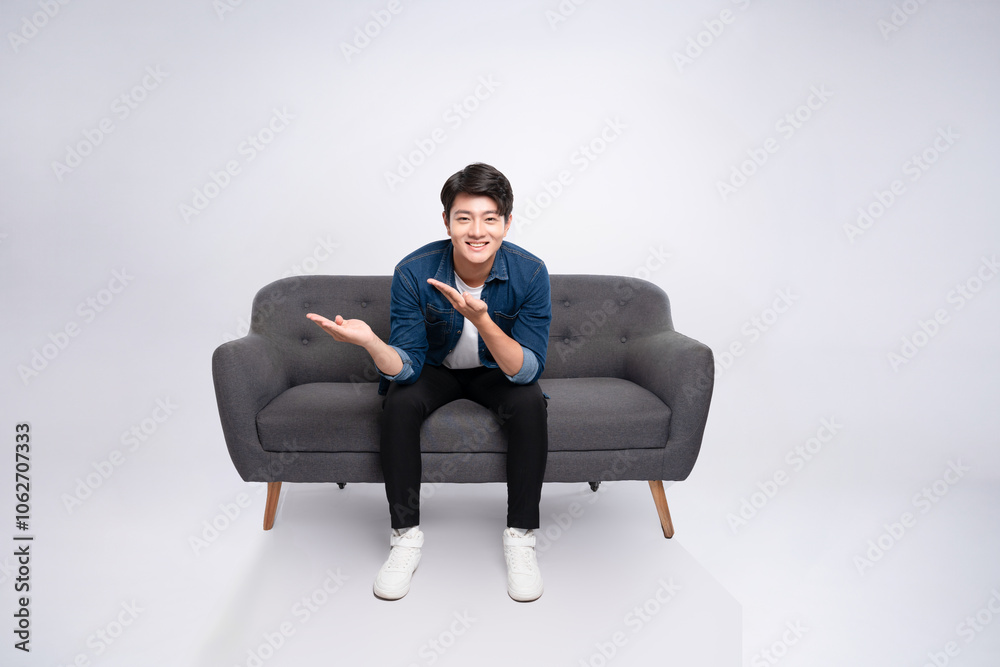 Full body image of young Asian man posing on sofa on white background Full body image of young Asian man posing on sofa on white background