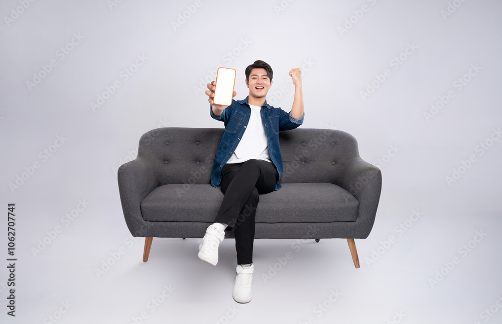 Full body image of young Asian man using phone sitting on sofa on white background