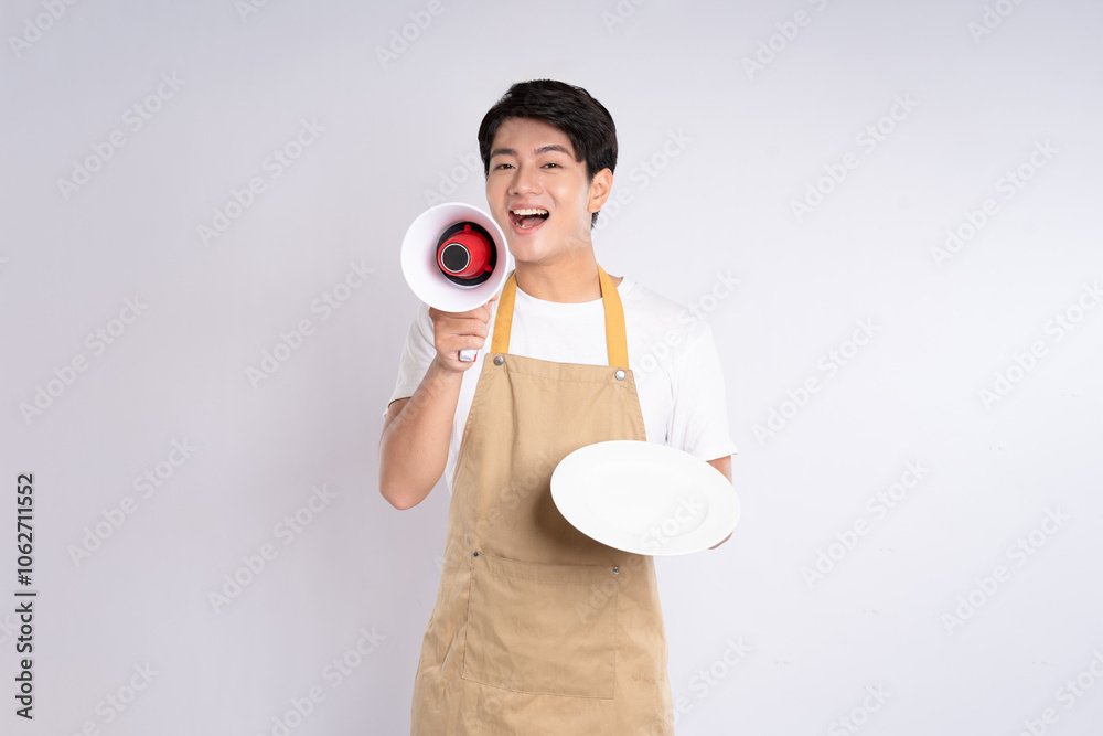 Portrait of young asian man wearing apron holding handspeaker and posing on white background Portrait of young asian man wearing apron holding handspeaker and posing on white background