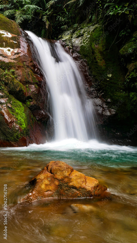 Gleweran is the name of this small waterfall, flowing from a cliff covered in green moss, with large rocks and tropical trees around it. Located in Mount Halimun Salak National Park, Bogor, Indonesia.