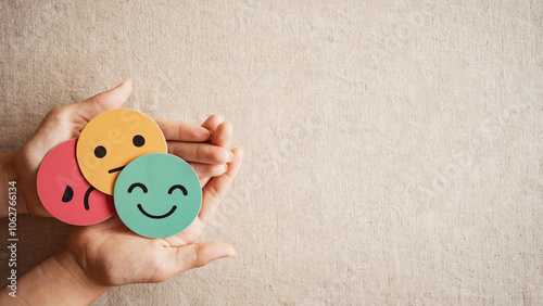Hands holding sad face hiding behind happy face, psychology and mental health, emotional intelligence concept