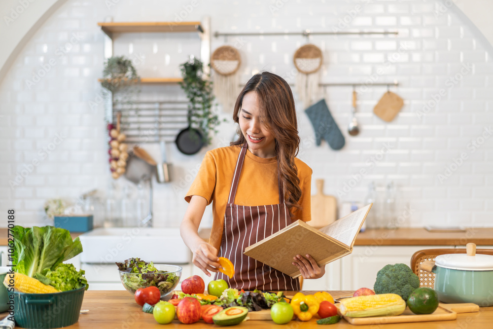 Asian young woman holds a book with online audience or simply enjoying the cooking process, health, fruit, freshness, and organic living, digital recipe platform, eating, healthy at kitchen Asian young woman holds a book with online audience or simply enjoying the cooking process, health, fruit, freshness, and organic living, digital recipe platform, eating, healthy at kitchen