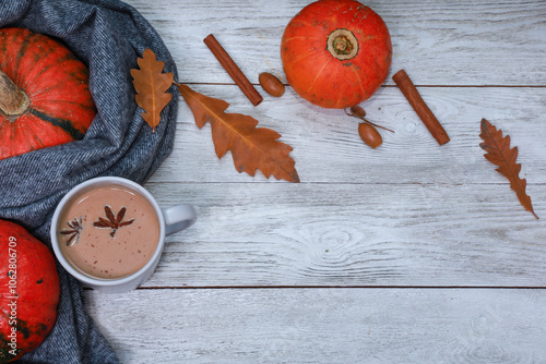 Spicy pumpkin latte in white wooden table with thanksgiving fall decoration, dry leaves, cinnamon, warm soft scarf. Coffee shop concept with autumn mood, top view, copy space