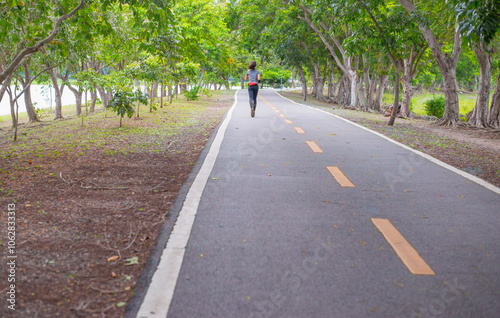 A person is jogging alone on the road in a park.