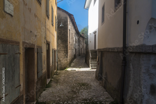 Un vicolo del borgo di Erto presso la diga del Vajont con la sua pavimentazione ad acciottolato passa fra alcune case in una giornata di sole photo