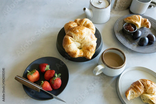 Breakfast table with croissants, coffee, strawberries, and plums photo