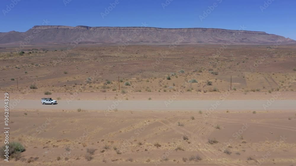 Aerial: Side follow of a white pickup car driving on a straight desert dirt road in Namibia, Africa Aerial: Side follow of a white pickup car driving on a straight desert dirt road in Namibia, Africa