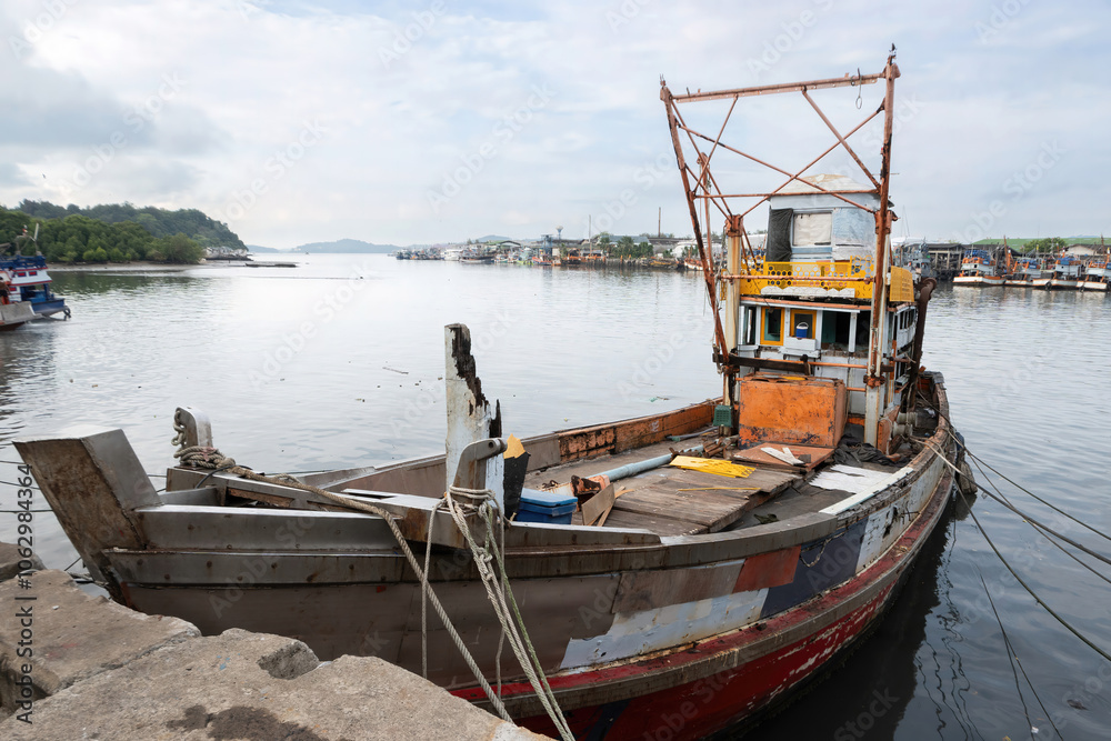 A colorful traditional wooden fishing boat, equipped with tools and gear, is docked at the local fishing pier, transporting fish from the boat to the market in Phuket, Thailand. A colorful traditional wooden fishing boat, equipped with tools and gear, is docked at the local fishing pier, transporting fish from the boat to the market in Phuket, Thailand.
