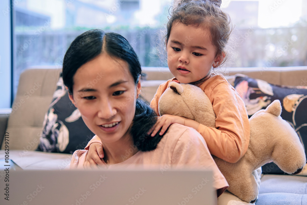 Daughter looking at mother using laptop in living room at home