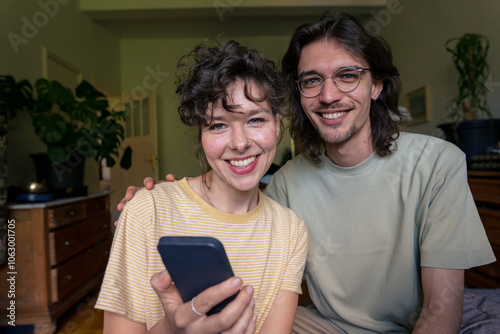 Happy young woman holding smart phone near boyfriend at home photo