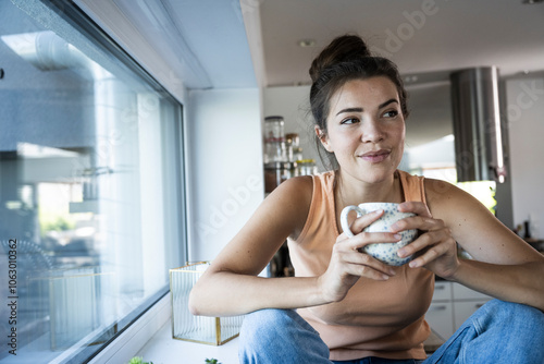 Thoughtful woman sitting with coffee cup in kitchen at home photo