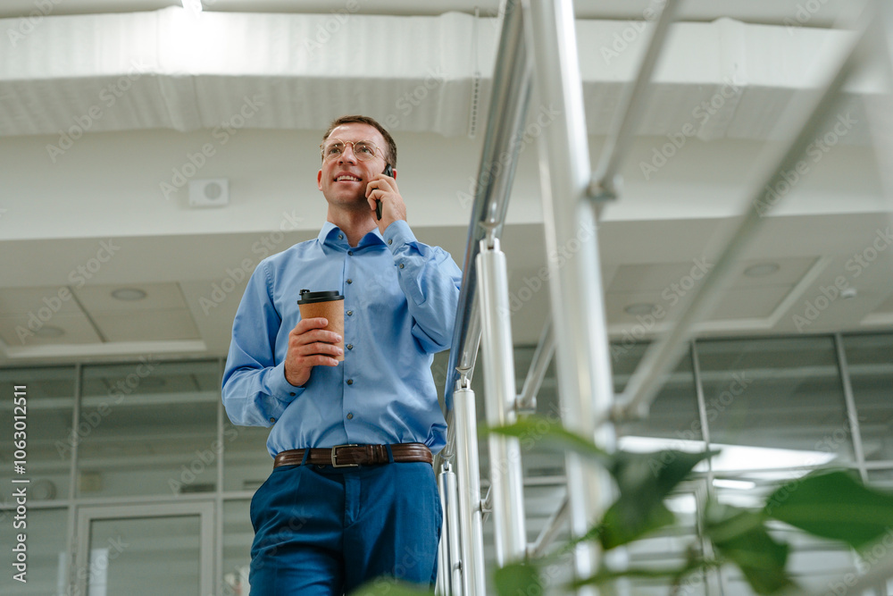 Businessman talking on smart phone near railing in office Businessman talking on smart phone near railing in office