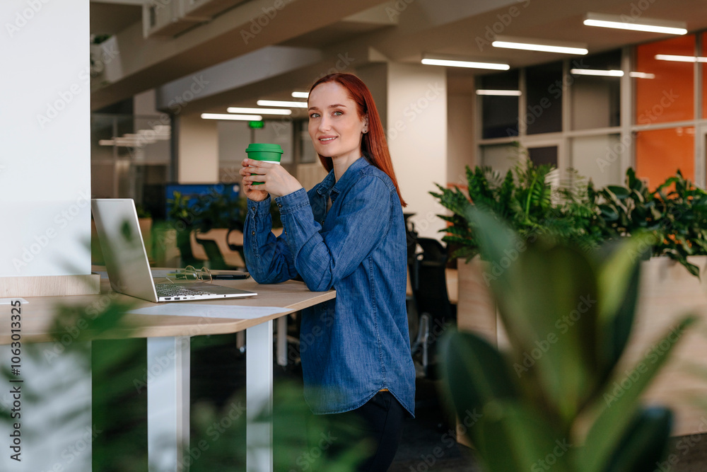 Smiling redhead entrepreneur having coffee at work place Smiling redhead entrepreneur having coffee at work place