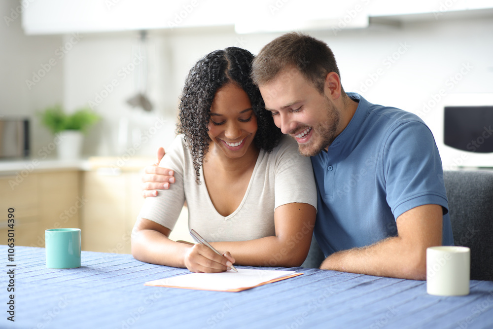 Happy affectionate couple signing contract in the kitchen Happy affectionate couple signing contract in the kitchen