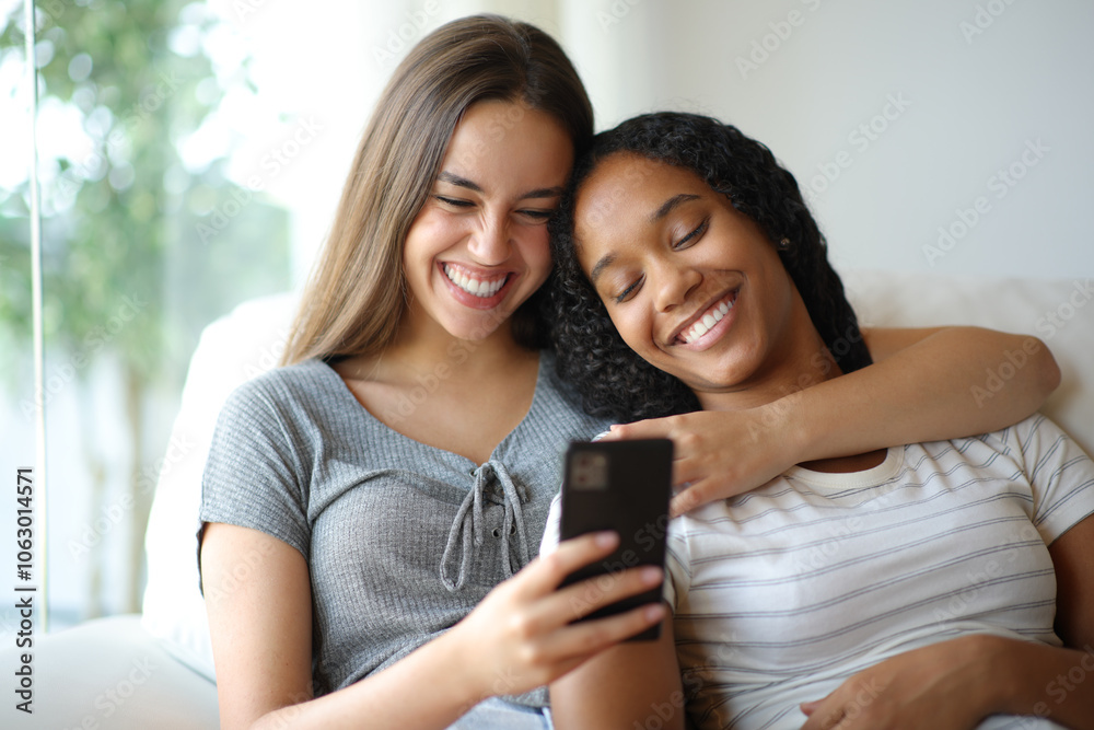Happy interracial lesbian couple checking cell phone on a sofa Happy interracial lesbian couple checking cell phone on a sofa
