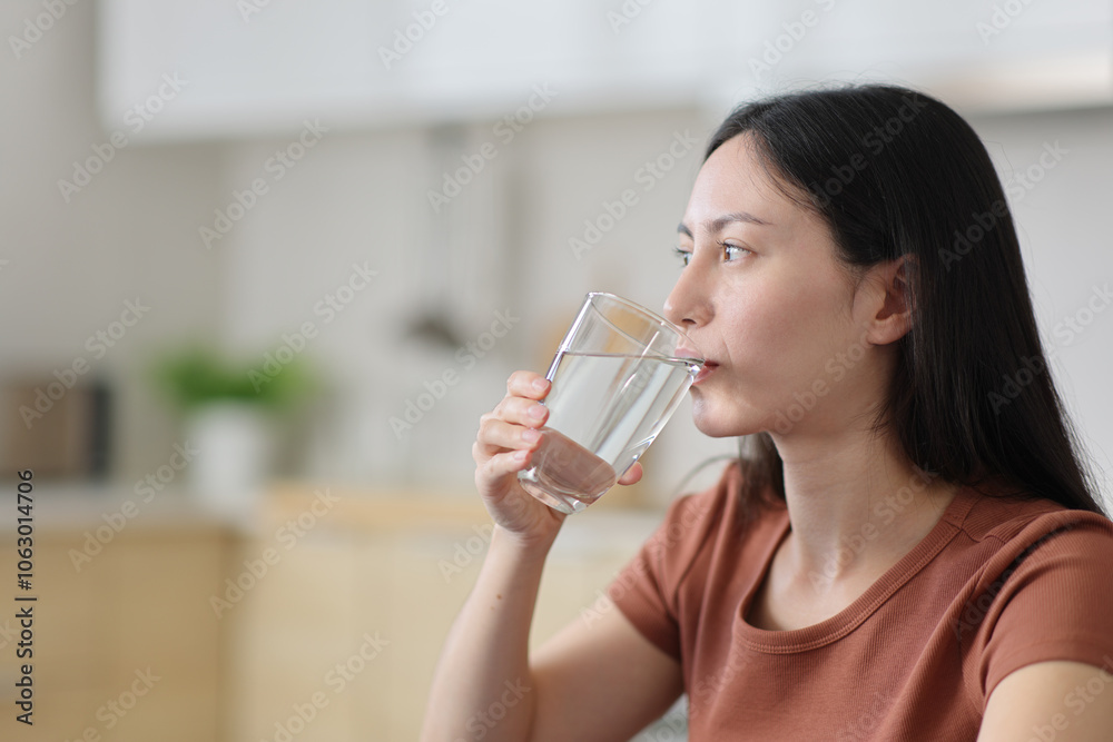 Asian woman drinking tap water from glass in the kitchen Asian woman drinking tap water from glass in the kitchen