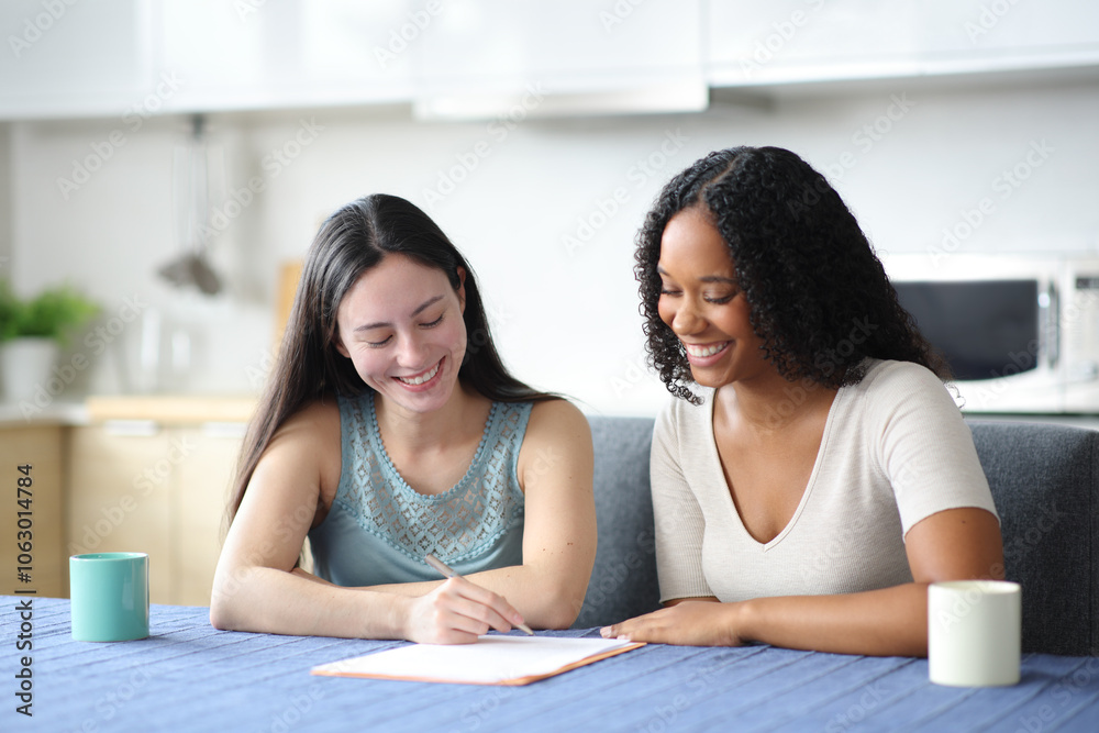 Happy interracial roommates signing paper contract at home Happy interracial roommates signing paper contract at home