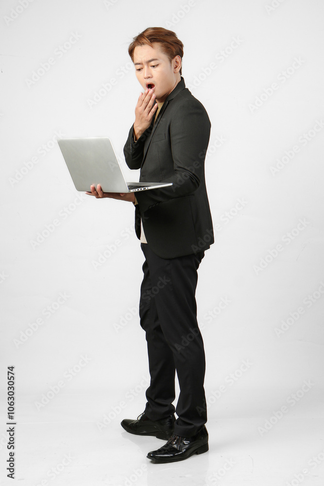 full lenght shoot of pensive asian business man wearing suit holding laptop computer with surprised shocked expression on isolated background full lenght shoot of pensive asian business man wearing suit holding laptop computer with surprised shocked expression on isolated background