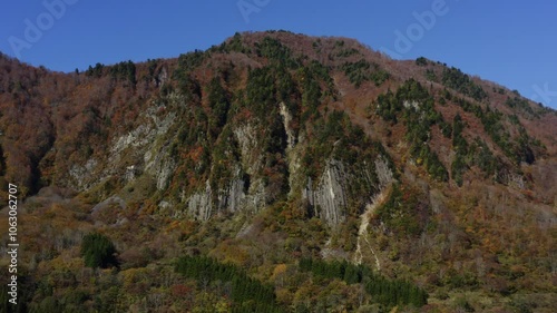 ドローン映像：太陽の光を浴びている、鮮やかに紅葉した山と壮大な柱状節理 photo