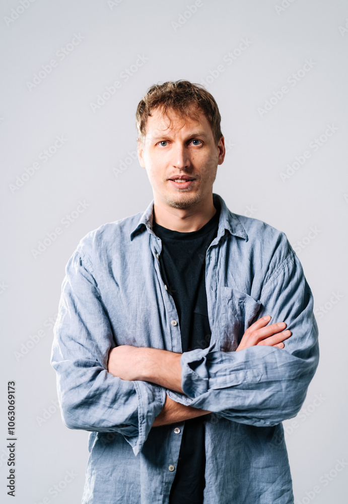 Tattooed man poses confidently in gray. A young man stands with arms crossed, wearing a casual shirt, exuding confidence in a neutral setting. Tattooed man poses confidently in gray. A young man stands with arms crossed, wearing a casual shirt, exuding confidence in a neutral setting.