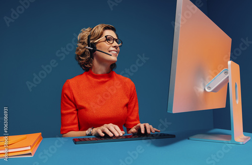 Mature woman in eyeglasses and headset working at desk while communicating photo