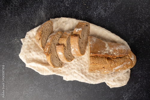 Artisan sliced bread in rustic style, arranged neatly on a dark, textured surface that adds a contrast highlighting the bread's crust and crumb textures vividly. photo