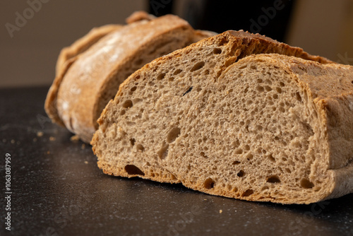 Artisan sliced bread in rustic style, arranged neatly on a dark, textured surface that adds a contrast highlighting the bread's crust and crumb textures vividly. photo