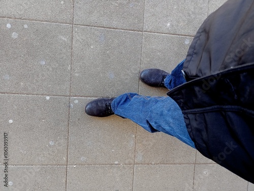 Down look of a male and his shoes on the asphalt ground.